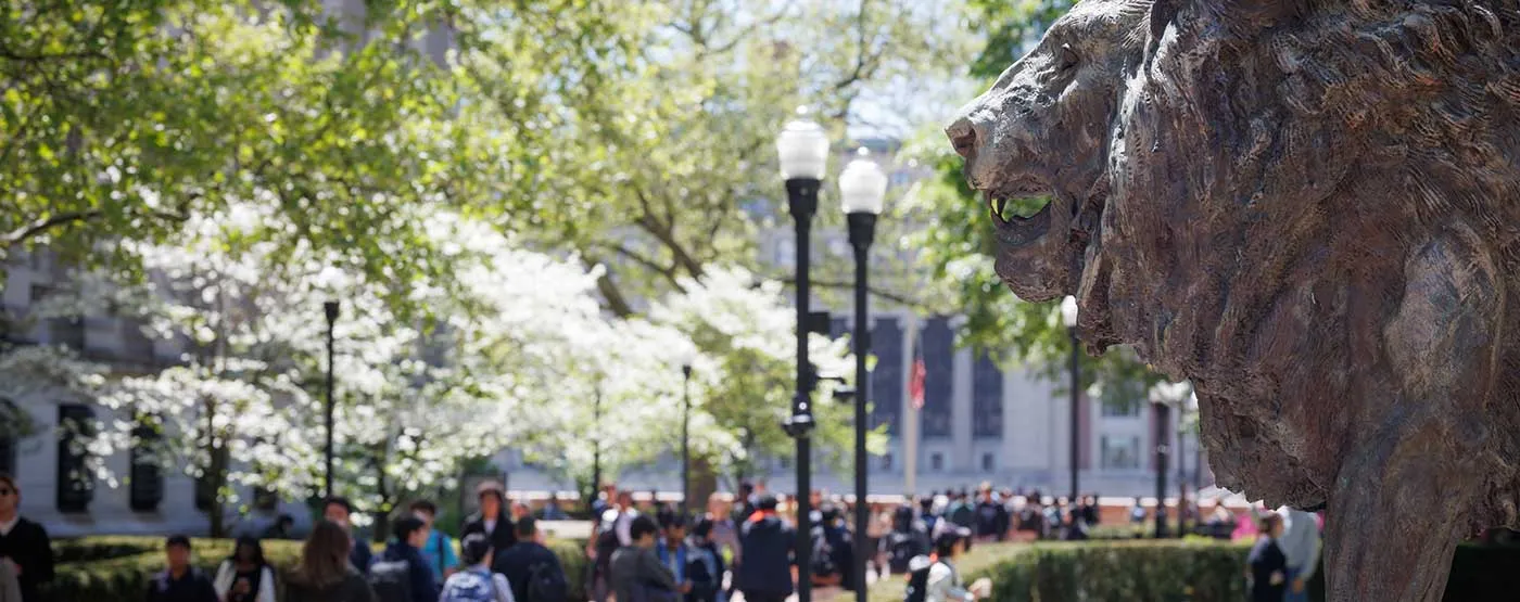 Campus statue of lion with students walking on campus