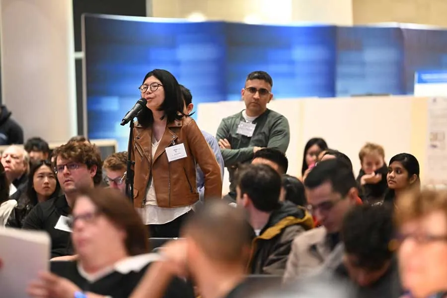 photo of audience, with one woman asking a question at a mic 