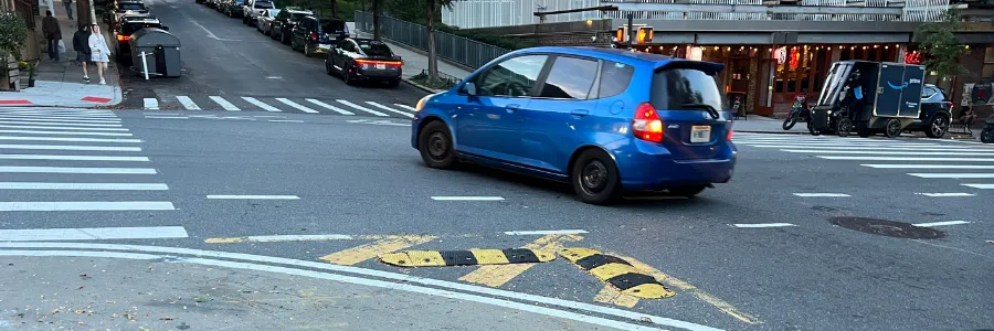 Image of a blue vehicle turning past traffic calming bumpers mounted to the asphalt.