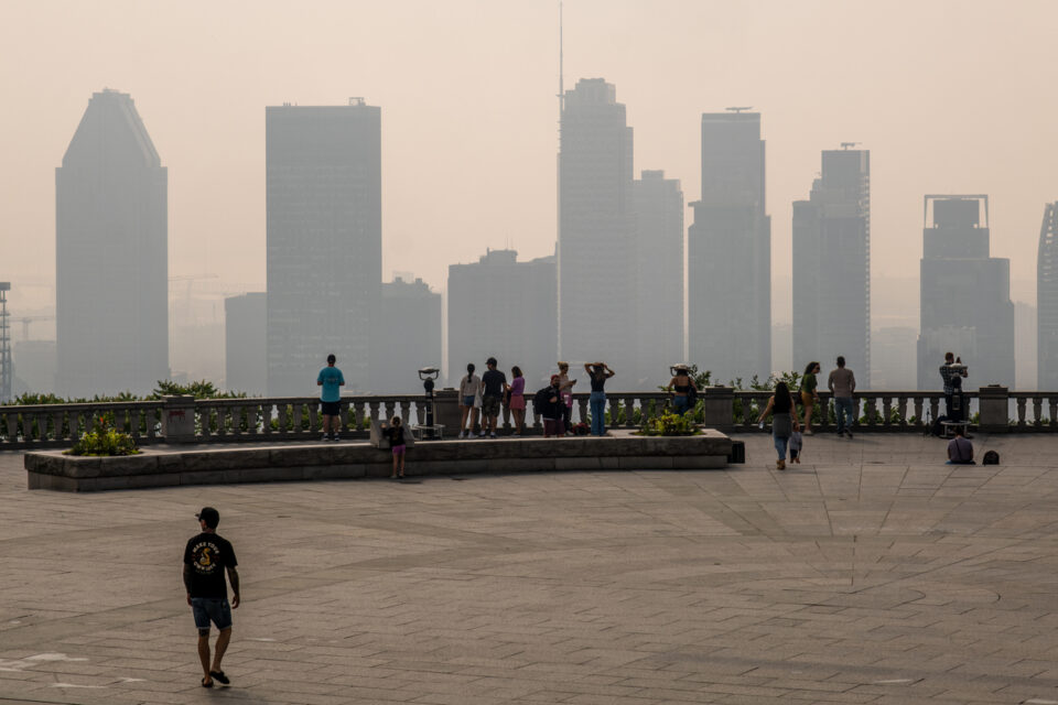 People standing in front of the Montreal skyline in a haze of wildfire smoke